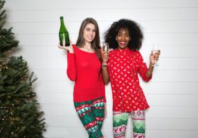 Two women holding a champagne bottle and flutes beside a Christmas tree